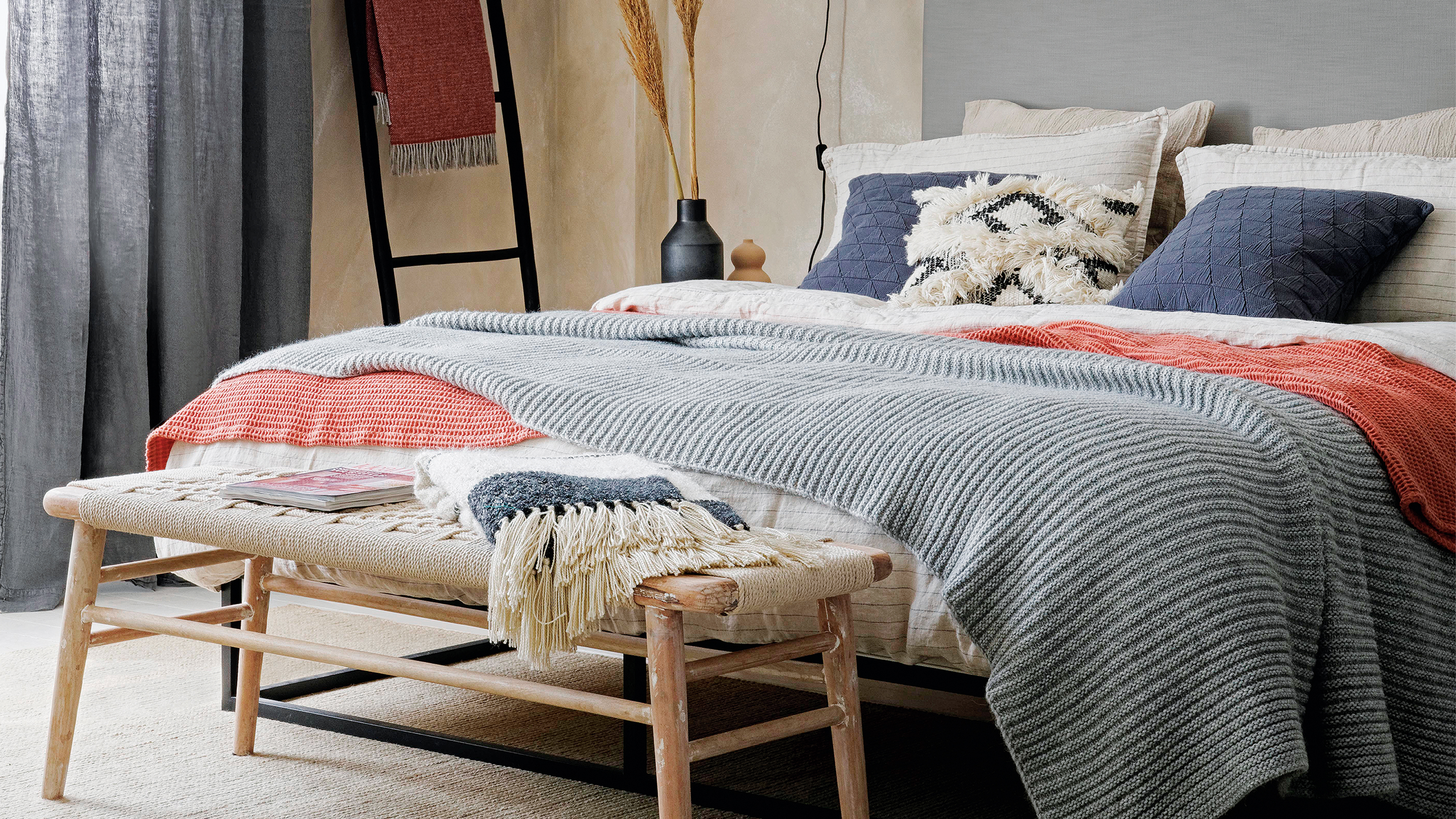 A bedroom with a bench at the bed of the bed