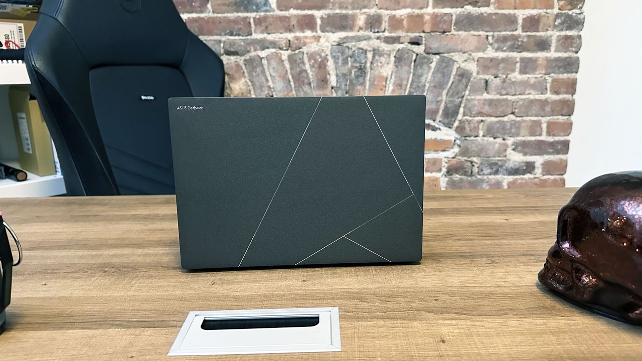 Asus Zenbook S 14 resting on a wooden desk open to show the large stylized Asus logo on its lid.