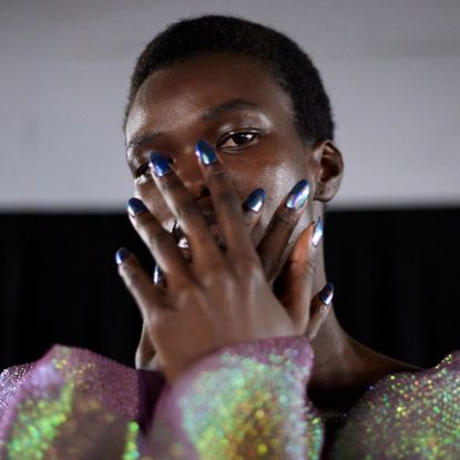 A model wearing an iridescent top holds a fresh manicure up to her face.