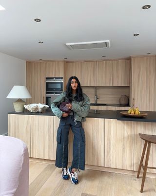 @monikh wears tri-colour trainers with cargo trousers and a cropped green jacket whilst in her wooden, modern kitchen