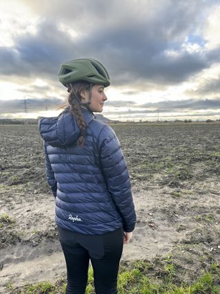 Woman stands looking away from camera towards muddy field. Jacket is navy blue.