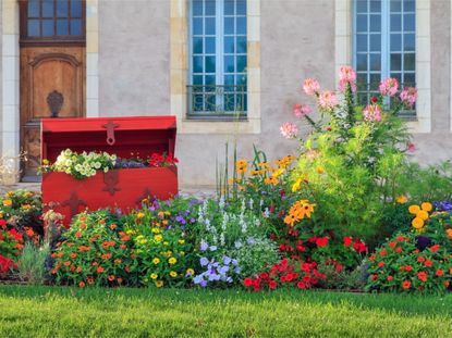 A red chest in a bed full of colorful blooming flowers