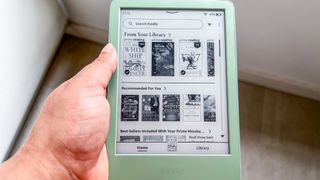 A hand holding the Amazon Kindle 2024 with the Home screen displayed