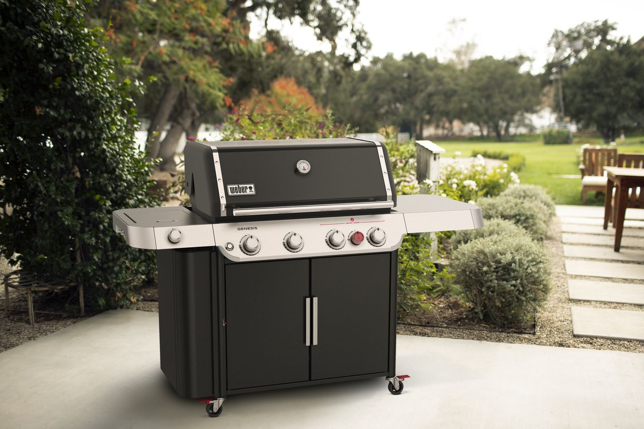 A gas grill on a patio next to a lawn