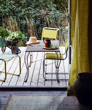 Small garden ideas showing a tiny deck with a small table and colourful outdoor dining chairs.
