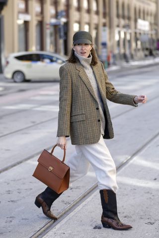 woman wearing blazer, turtleneck, white pants, cap, and cowboy boots