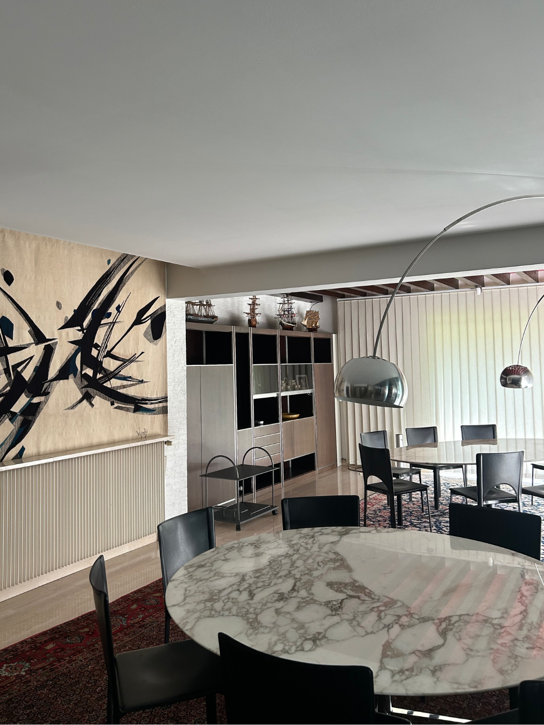 Roset family dining room with marble tables, black chairs, chrome arc lamps and bold abstract art.