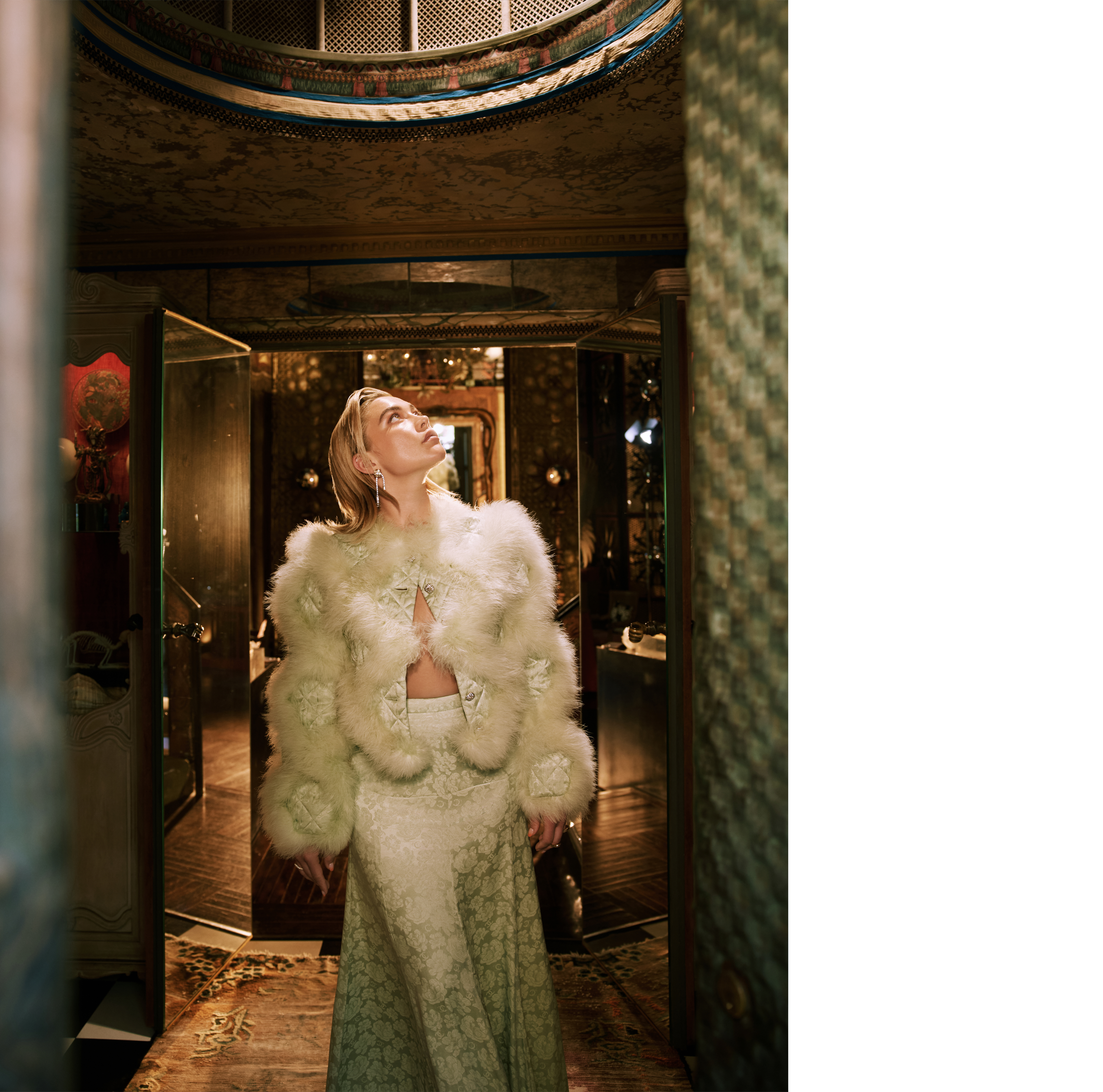Florence Pugh standing in the entryway of the Tony Duquette house in Beverly Hills. She is looking up and wearing a mint green Chanel coat with furry detailing and a mint green skirt with floral detailing.