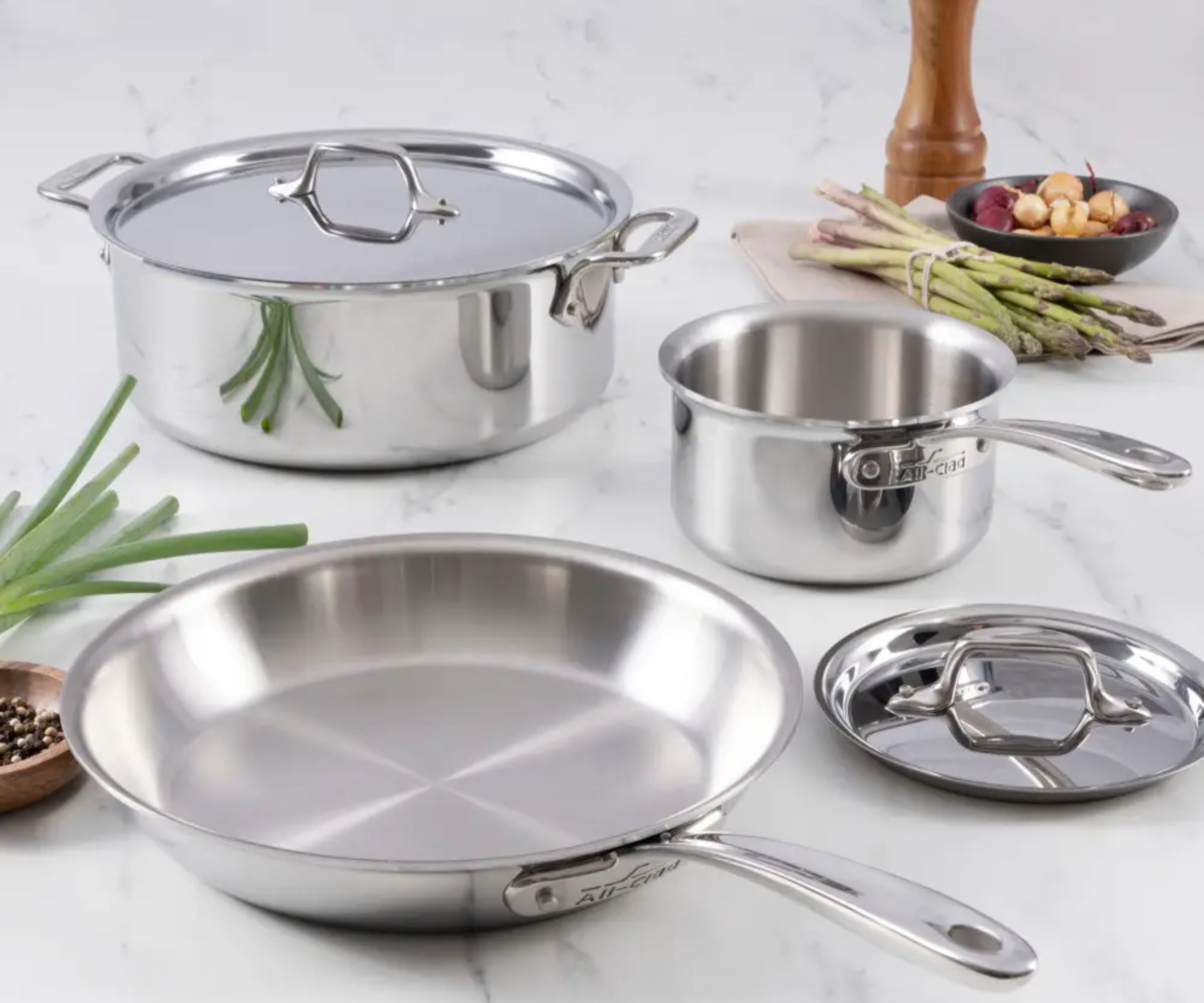 A set of three stainless steel frying pans on a marble countertop.