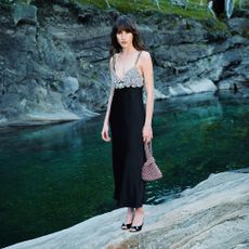 A female model wearing a black, diamond dress from ThedoubleF, standing by a river.
