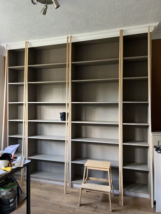 A living room with bare built-in shelving painted a beige color with moldings fixed to the middle panels