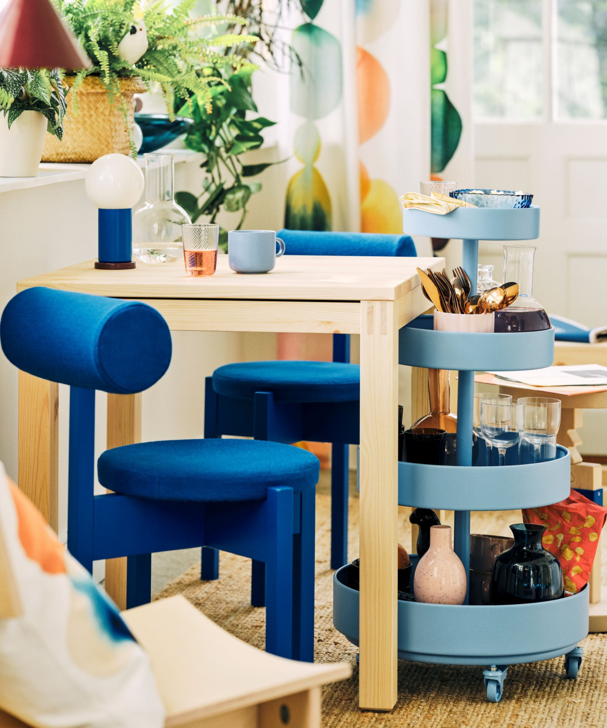 a small wooden table, a blue modern chair, and a blue rolling cart from IKEA's PS collection