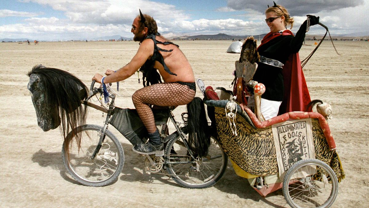 A woman being towed in a chariot by a man on a bicycle at Burning Man