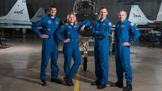 four astronauts in a row in front of an airplane and with nasa airplanes in the background