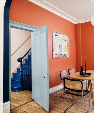 dining room with orange walls and a light blue paint door, with exposed floor boards and a wooden dining table
