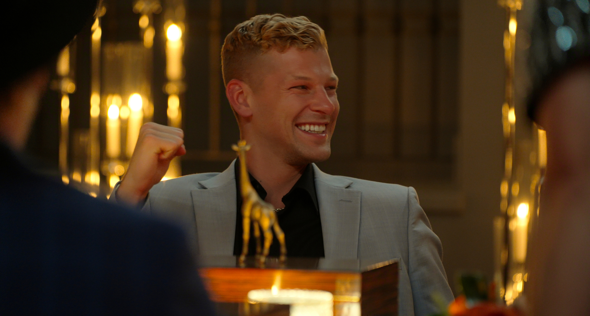 million dollar secrt season 2 winner nick pellechia smiles and holds up his fist at the main table in the stag as the cast looks through their boxes