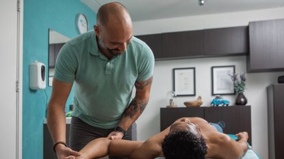 Man lies on treatment table while other man holds his shoulder and wrist