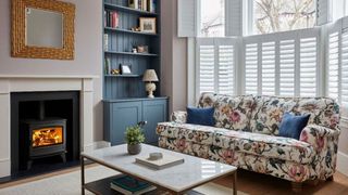 cosy living room with log burning stove and white shutters and floral sofa with marble coffee table