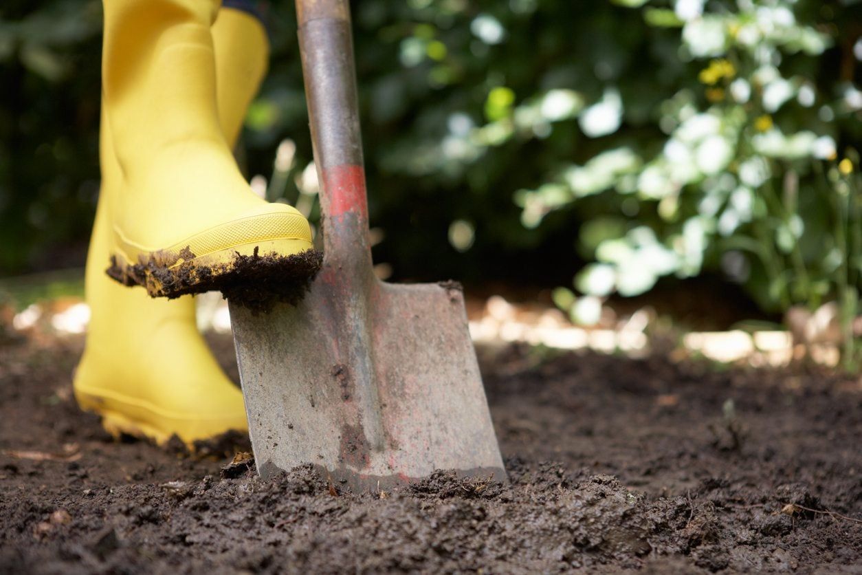 Person With Yellow Rain Boots Shoveling In The Garden