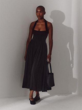 a photo of a woman wearing a black halter dress with a matching shoulder bag and Mary Jane flats