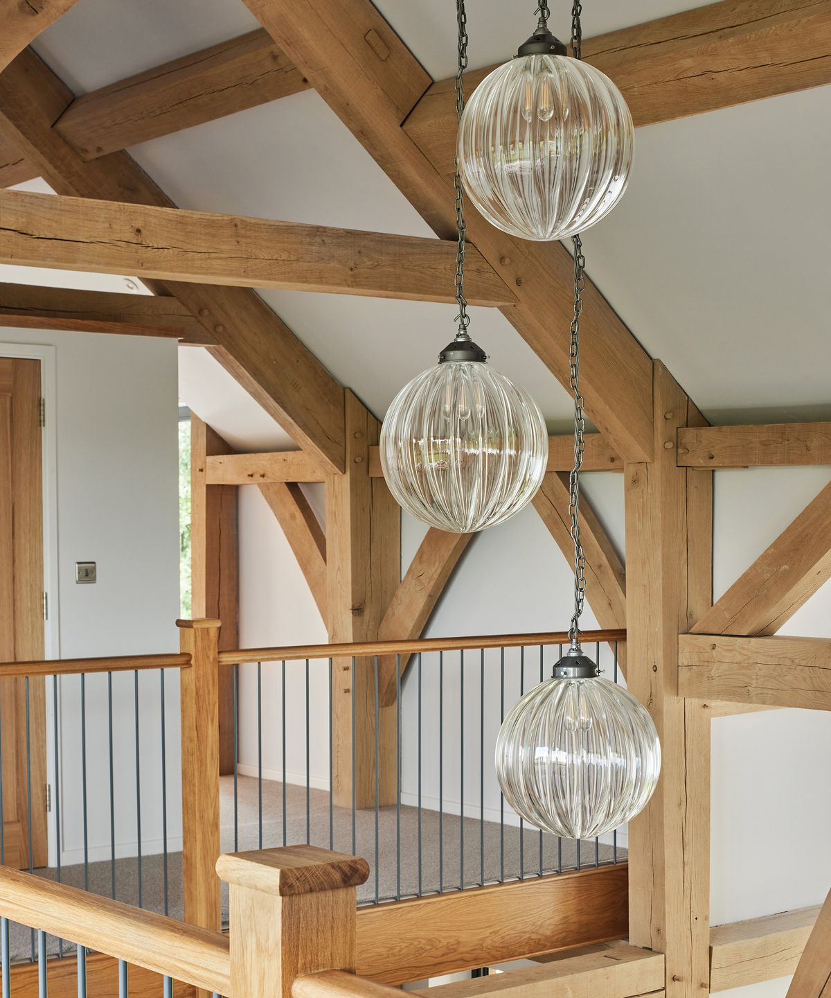 A landing which looks down onto an open atrium ground-floor. There are three pendant lights and lots of exposed oak