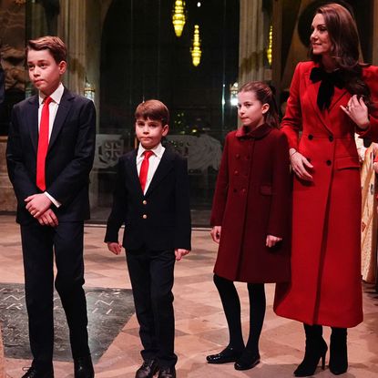 Prince George, Prince Louis, Princess Charlotte and Kate MIddleton wearing suits and red coats standing in Westminster Abbey