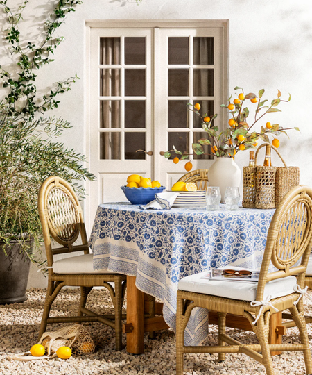 an al-fresco tablescape with a blue tablecloth, lemons in a bowl, and a rattan wine holder