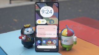 Der Homebildschirm des Google Pixel 7 Pro, welches neben zwei Androiden-Figuren steht