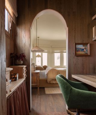 Wood panelled snug office with green velvet armchair, wooden desk and arched doorway