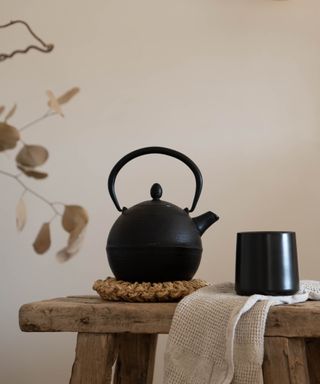 Black coffee mug on a wooden side table beside a matching black teapot