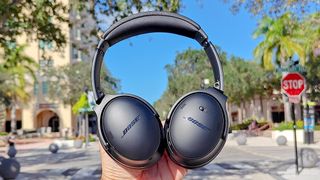 Hero image for best Bose headphones showing Bose QuietComfort headphones held up against a blue sky