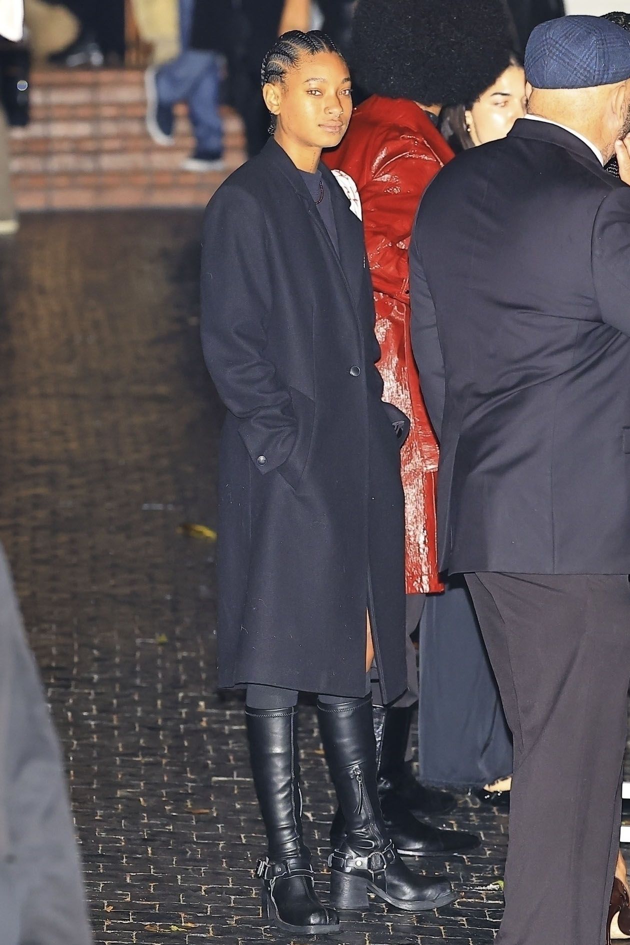 Willow Smith wearing a black coat, black boots, and short sweater dress