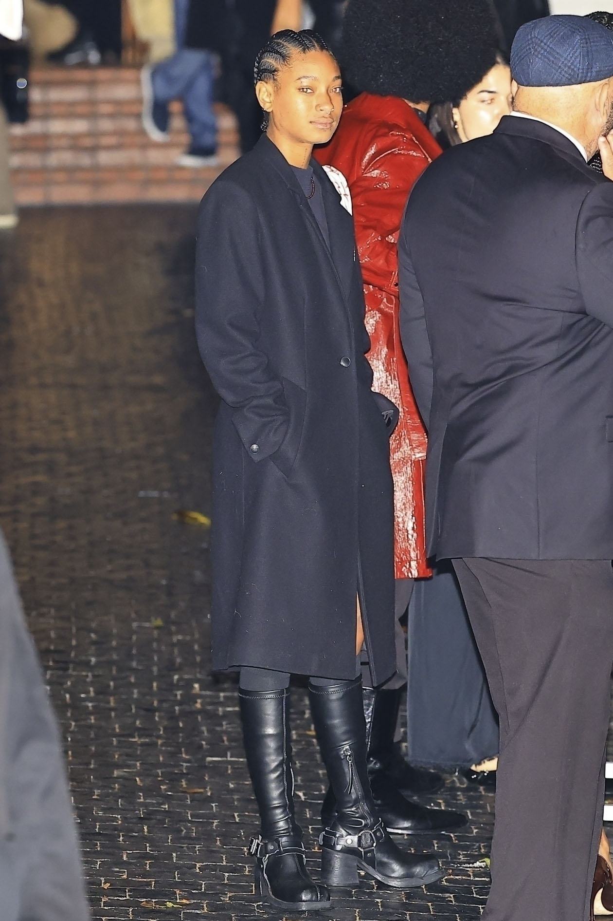 Willow Smith wearing a black coat, black boots, and short sweaterdress.