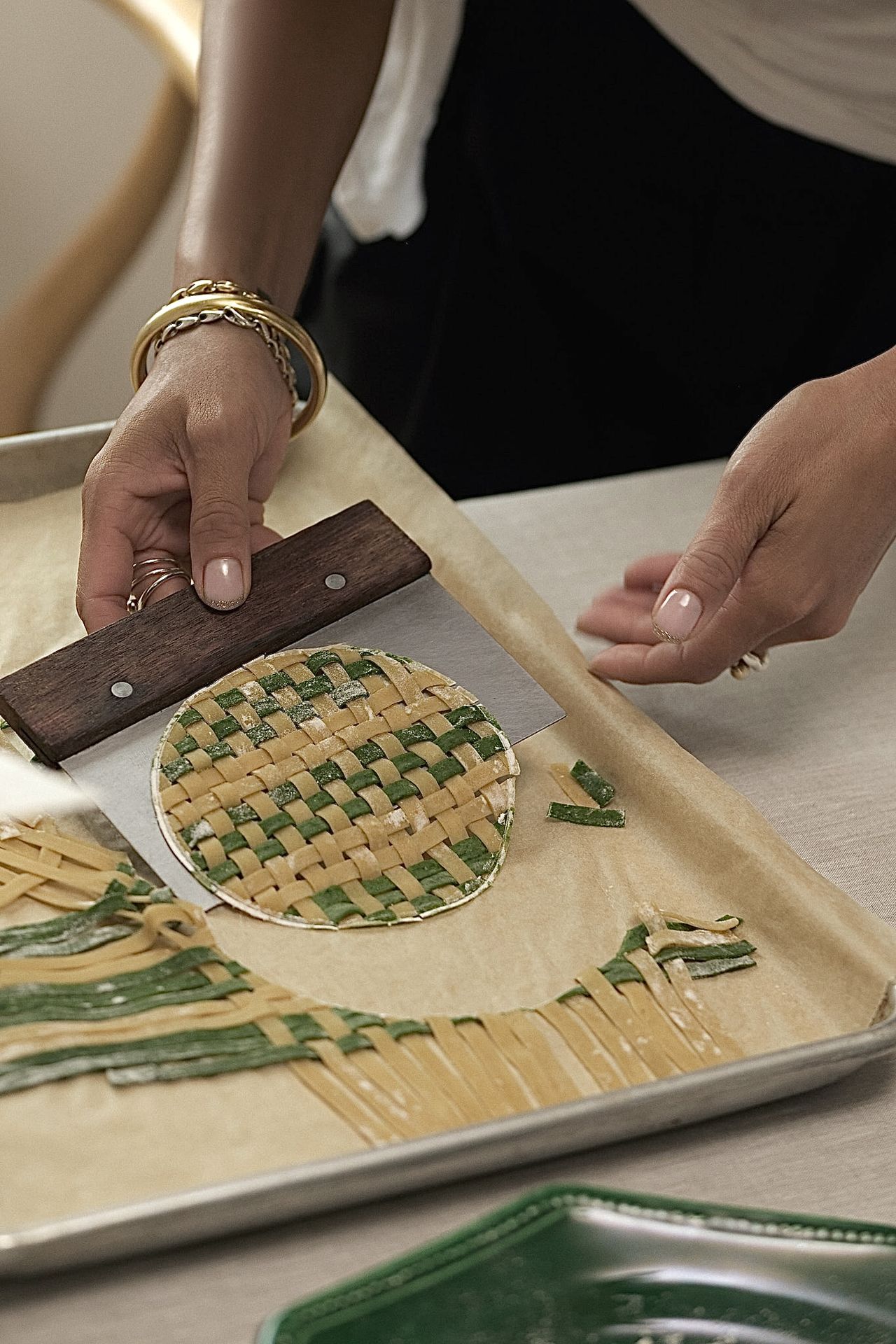 A woman handles a pasta-made, woven round "tapestry" in yellow and green shades as she takes it out of a silver tray.