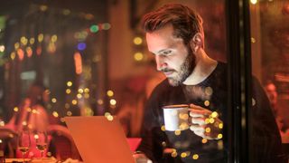 Man holding cup and using laptop in cafe