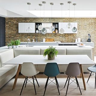 kitchen diner with pale leather bench seating, white dining table with coloured chairs and French door out to the garden