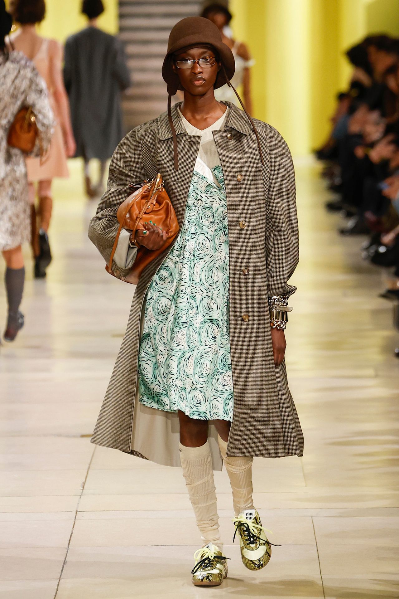 Model walking in the F/W 25 Miu Miu show during Paris Fashion Week wearing a plaid car coat with a floral dress.