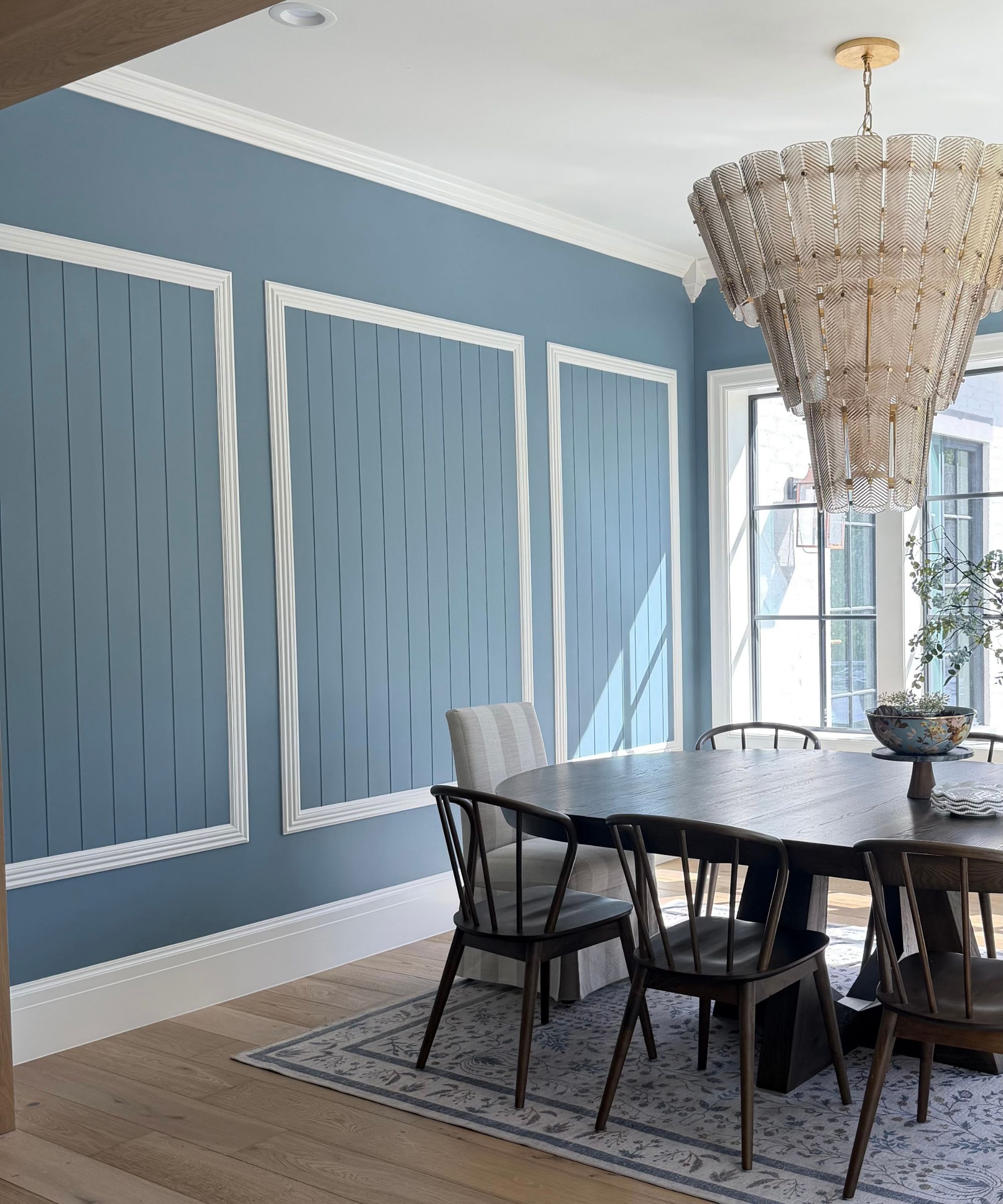Dining room painted in powder blue (Cottage Door by Valspar), a dark-wood oblong dining table with wooden spindle chairs, a Persian-style rug beneath, and a large glass chandelier.