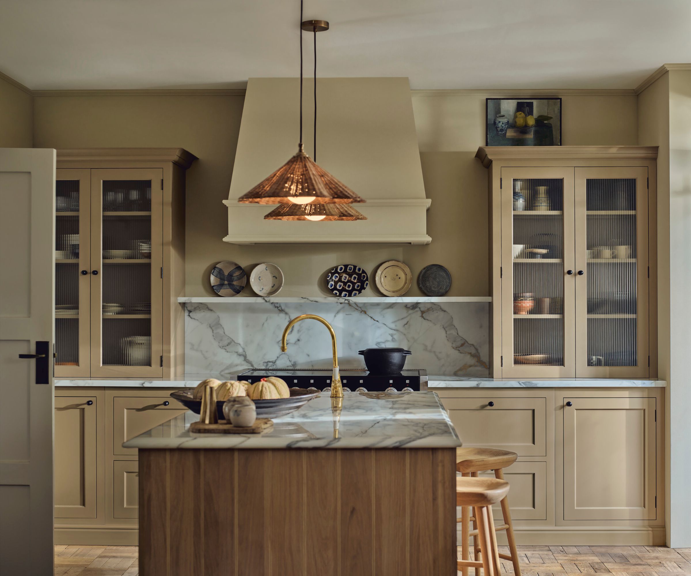A neutral kitchen with marble counters and plates displayed on a narrow shelf above the cooktop