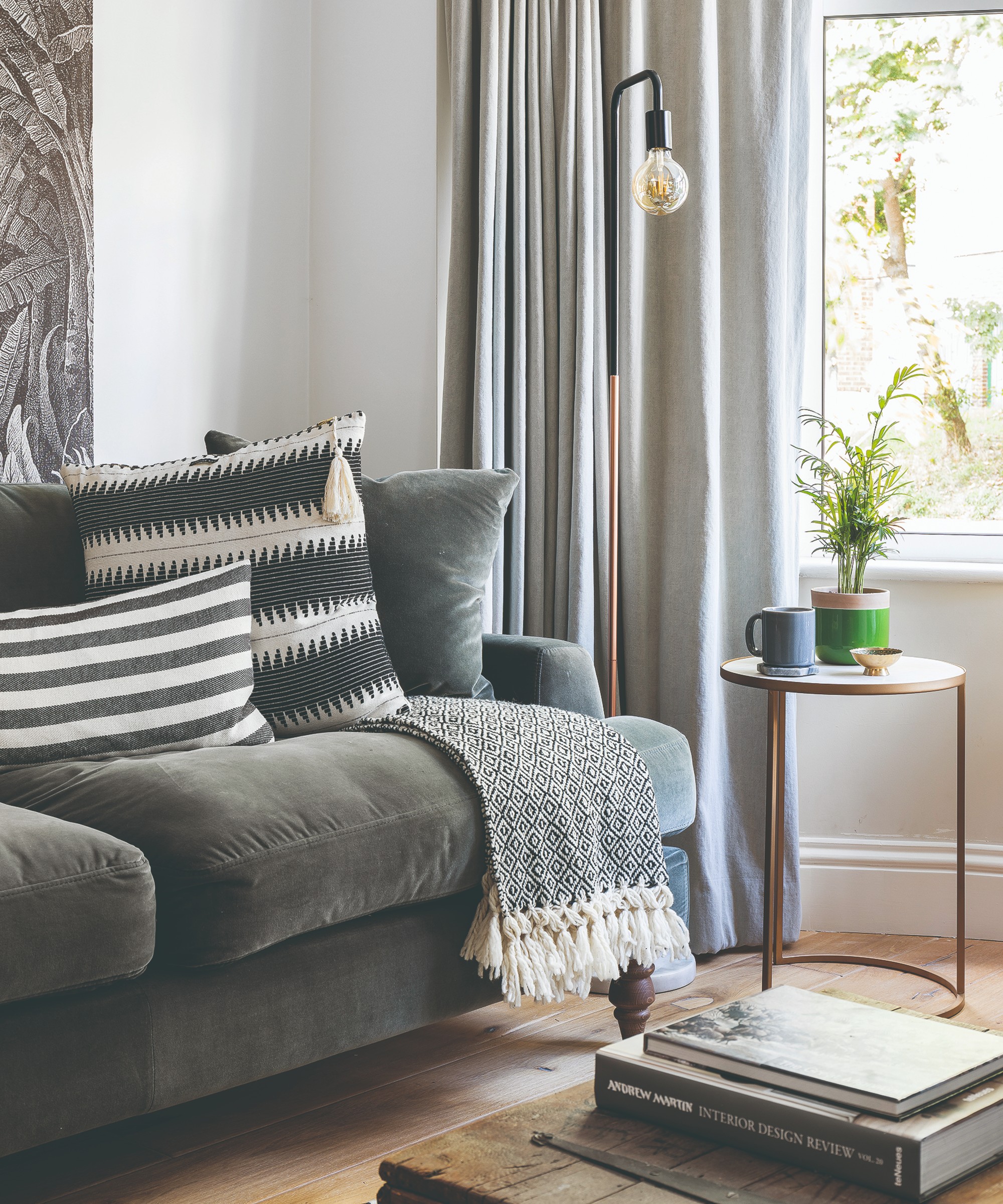A white-painted living room with a dark grey velvet sofa, light grey curtains and a grey tapestry on the wall