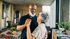 A smiling older couple dance together in their kitchen.