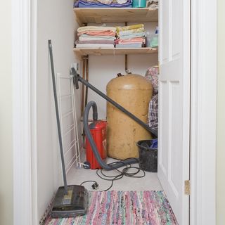 laundry cupboard with cloths on shelf vacuum cleaner and cream colour cylinder