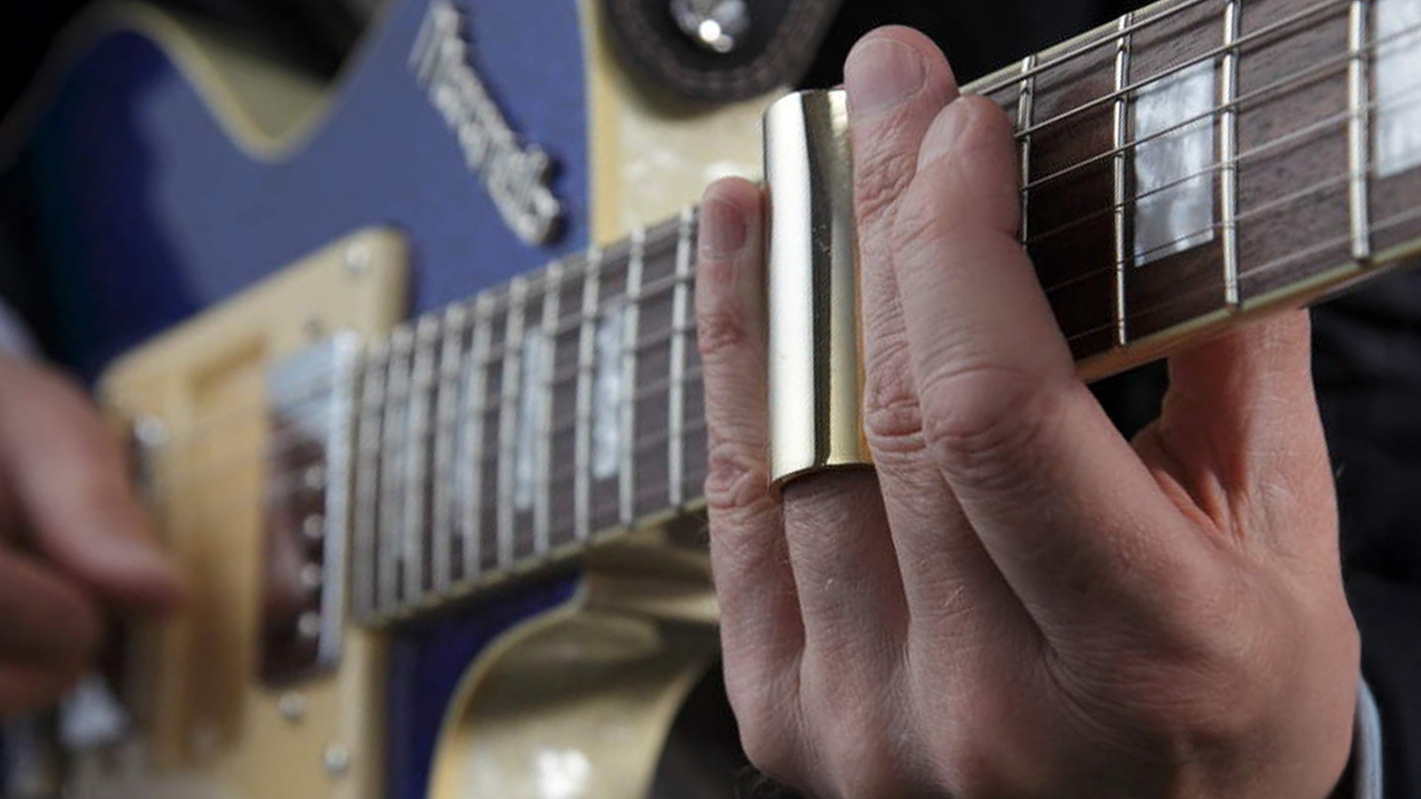 Man playing electric guitar with a brass slide