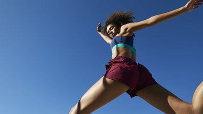 Frizzy young female athlete jumping against clear blue sky on sunny day