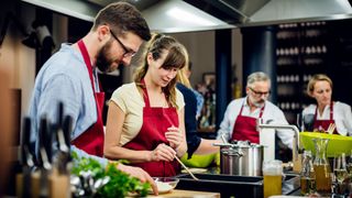 Group of adults wearing red aprons taking part in cookery class