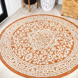 A white and orange round rug features a vintage-inspired pattern