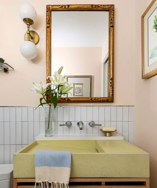 A light pink bathroom with a gold rectangular mirror above the sink