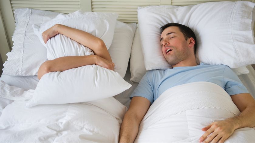 A man sleeping on his back snoring next to his partner who&#039;s covered her head and ears with a pillow