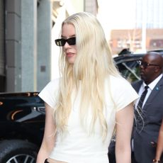 Anya Taylor-Joy wearing a white T-shirt, black low-rise trousers, and black pointed-toe heels 