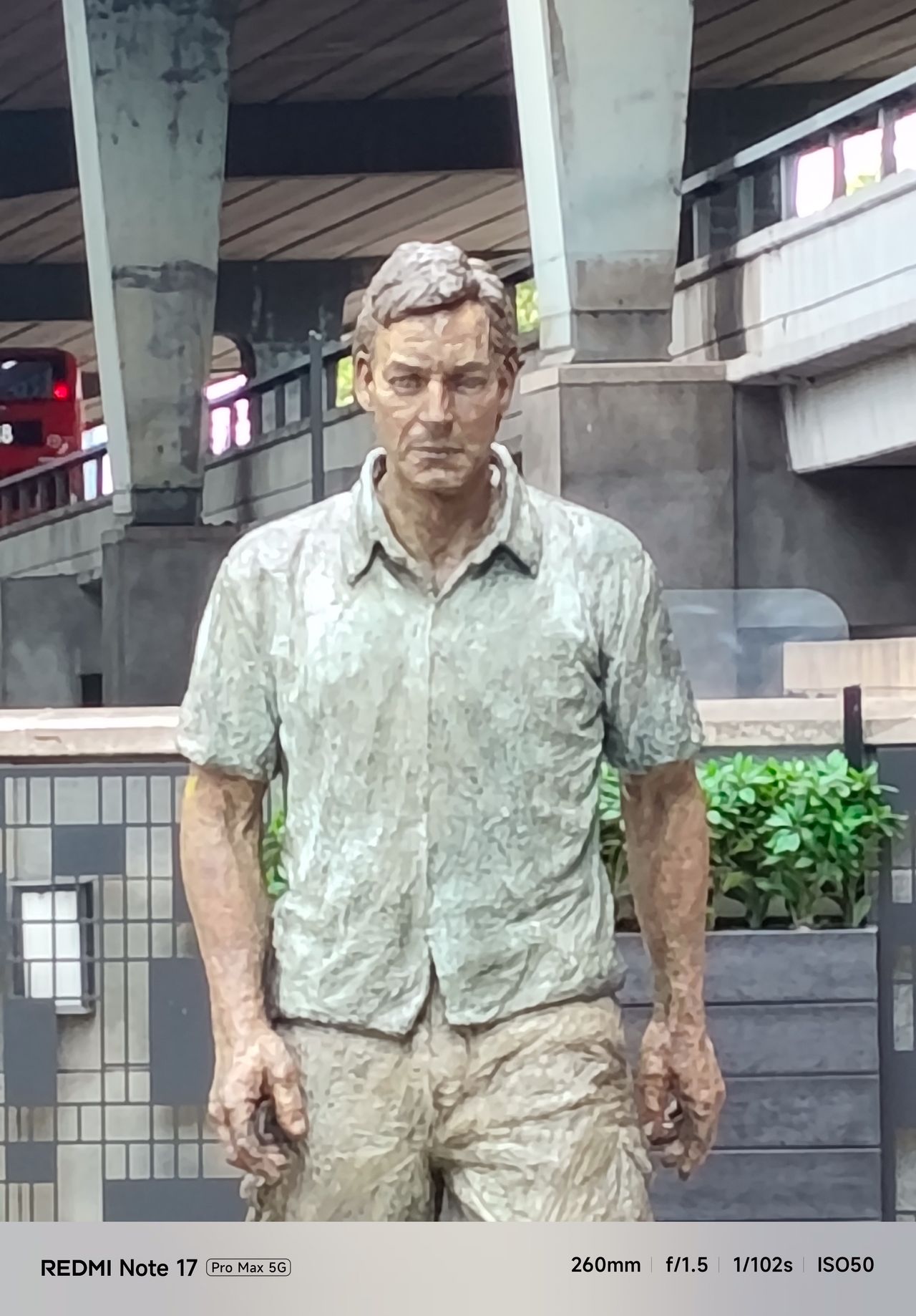 Close view of a walking man sculpture beneath an elevated roadway, photographed at 10x zoom.